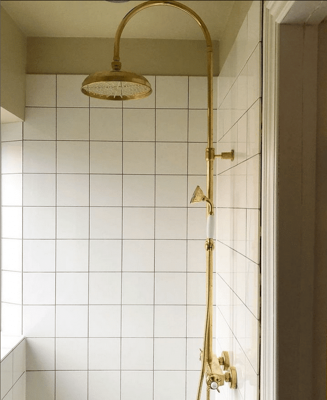 hvide vægfliser og guld brusearmatur på badeværelse